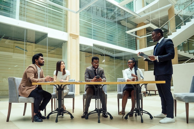 Hommes d'affaires afro-américains bien habillés faisant un rapport aux employés subalternes dans un bureau moderne