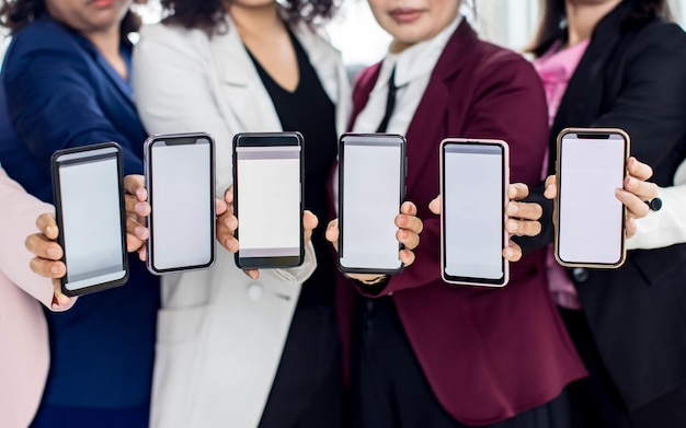 Des hommes d'affaires assis ensemble au bureau sur un bureau avec un graphique coloré et des graphiques pater, tiennent des smartphones dans différents modèles avec des écrans vierges.