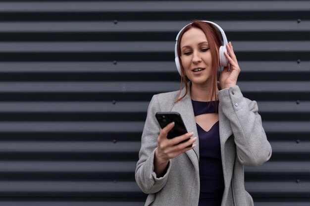 Hommes d'affaires aux cheveux roux sur des écouteurs près d'un mur gris écoutant de la musique au téléphone