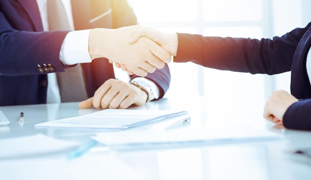 Photo des hommes d'affaires ou des avocats se serrant la main finissant une réunion ou une négociation dans un bureau ensoleillé. poignée de main et partenariat d'affaires.