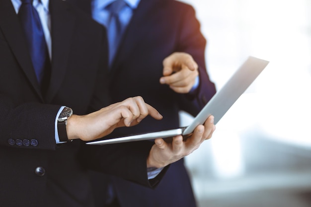 Des hommes d'affaires discutant d'une présentation lors d'une réunion, debout dans un bureau moderne ensoleillé. Un homme d'affaires inconnu avec un collègue cherchent des informations sur l'ordinateur portable, des avocats à la négociation.