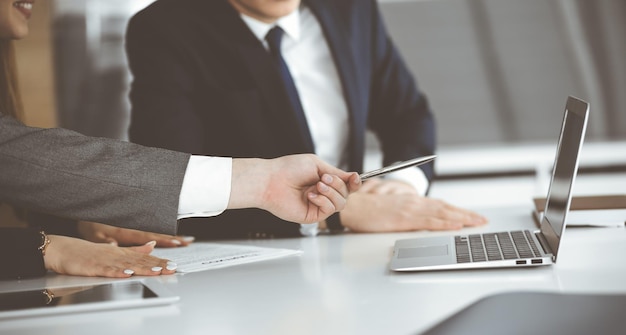 Des hommes d'affaires et une femme inconnus assis à l'aide d'un ordinateur portable et discutant de questions lors d'une réunion dans un bureau moderne en gros plan