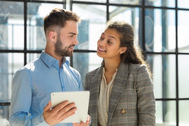 Les hommes d'affaires modernes travaillent à l'aide d'une tablette numérique et sourient en se tenant au bureau