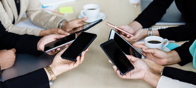 Des hommes d'affaires non identifiés et méconnaissables tenant une tablette tactile numérique vierge noire et des gadgets pour smartphone avec du texte de l'espace de copie ensemble autour de la table de travail dans le bureau de l'entreprise de la salle de réunion.