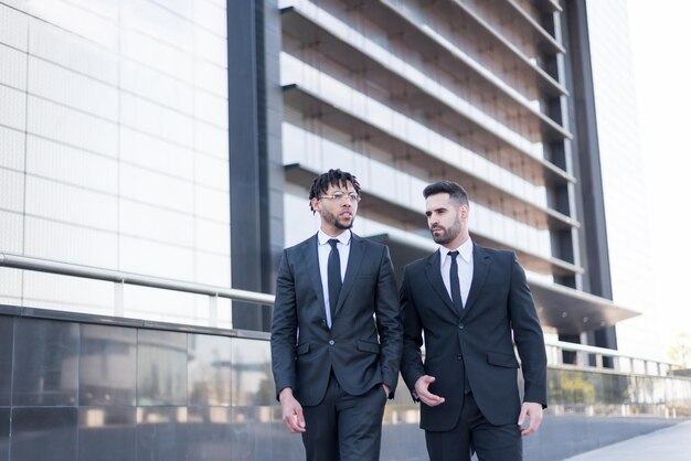 Hommes d'affaires portant des costumes marchant et souriant et parlant en plein air dans un quartier d'affaires