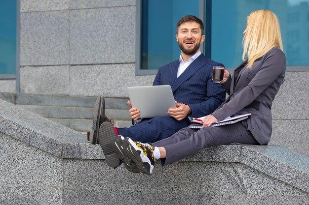 Des hommes d'affaires prospères, hommes et femmes, sont assis dans les escaliers d'un immeuble d'affaires avec des documents et un ordinateur portable dans les mains pour discuter de projets d'entreprise