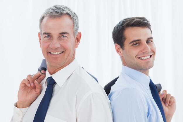 Hommes d&#39;affaires souriants posant dos à dos ensemble tout en tenant leur veste