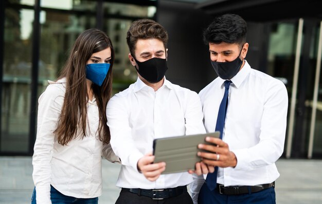 Des hommes d'affaires utilisant une tablette en plein air portant un masque de protection contre la pandémie de coronavirus COVID-19