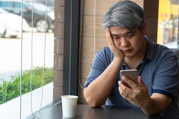 Hommes asiatiques d&#39;âge moyen (40 ans), stressés, fatigués et utilisant un smartphone