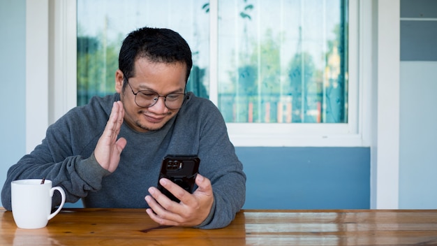 Hommes asiatiques portant des manches longues et des lunettes Assis et parlant sur un chat vidéo avec un smartphone. notion de communication.