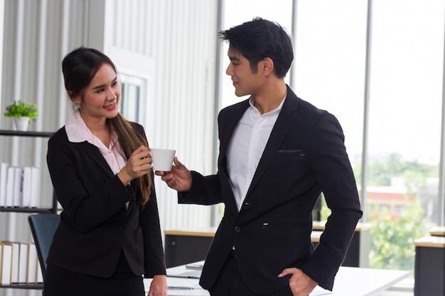 Hommes et femmes d'affaires asiatiques tenant une tasse de café blanc pendant la pause au bureau