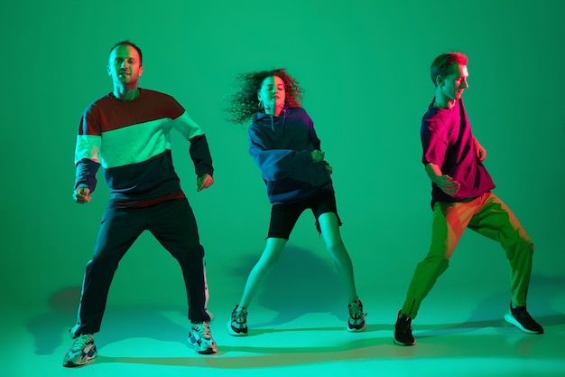 Hommes et femmes élégants dansant le hip-hop dans des vêtements lumineux sur fond vert à la salle de danse à la lumière du néon. Culture jeunesse, mouvement, style et mode, action. Portrait à la mode.