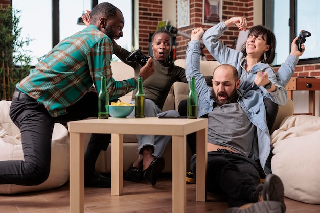 Des hommes et des femmes joyeux se sentent heureux de gagner des jeux vidéo, célébrant la victoire avec des bouteilles de bière et des boissons alcoolisées. Groupe de personnes s'amusant et profitant de la victoire à la fête à la maison.