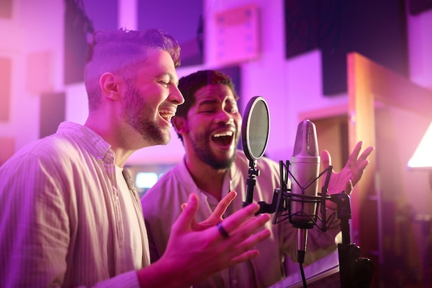 Les hommes font face ou chantent sur un microphone de studio au néon pour une chanson d'album ou un enregistrement radio dans la pratique nocturne Artiste chanteur musicien ou amis dans la production de médias vocaux sonores ou de collaboration avec une étiquette légère