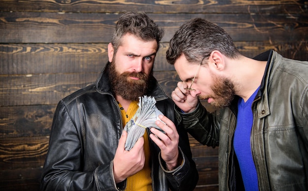 Les hommes hipster barbu brutal portent une veste en cuir et détiennent de l'argent liquide. Profit illégal et argent noir. Guy mafia dealer avec profit en espèces. L'homme brutal a de l'argent liquide. Affaires mafieuses. Bénéfice impressionnant.