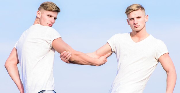 Hommes jumeaux musclés frères en chemises blanches fond de ciel Concept de fraternité Avantages d'avoir un frère jumeau Avantages et inconvénients d'avoir un frère jumeau identique Amitié et soutien