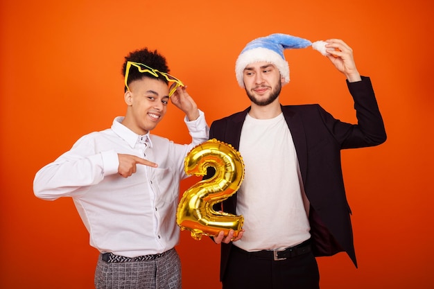 Des hommes multiculturels souriants portant un bonnet de Noel et des lunettes de grande étoile pointant vers le ballon numéro 2