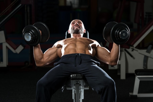 Hommes mûrs faisant des haltères inclinées Bench Press Workout In Gym