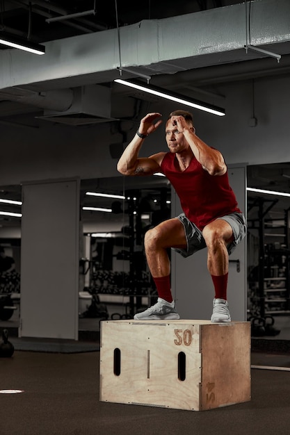 Hommes musclés sexy utilisant la plate-forme pour ses jambes sur un fond coloré foncé de gym