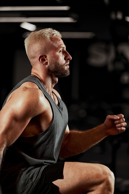 Hommes musclés sexy utilisant la plate-forme pour ses jambes sur un fond sombre et coloré de la salle de sport.