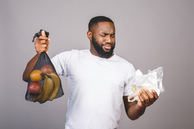 Les hommes noirs afro-américains tiennent un sac en filet avec des produits sans emballage en plastique isolé sur fond gris.