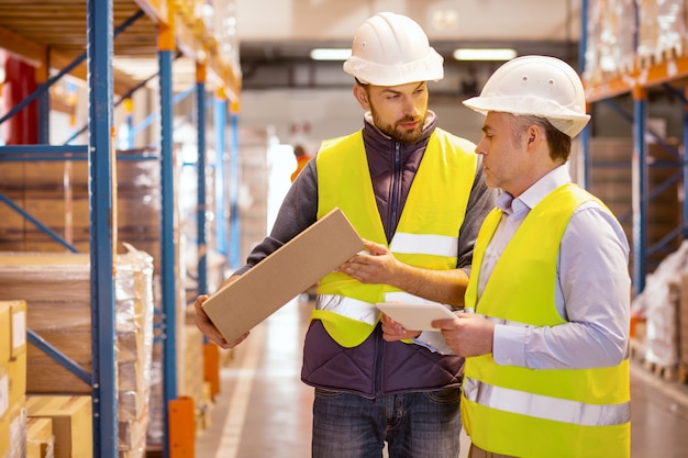 Hommes professionnels sérieux travaillant ensemble lors de la préparation des marchandises pour l'expédition