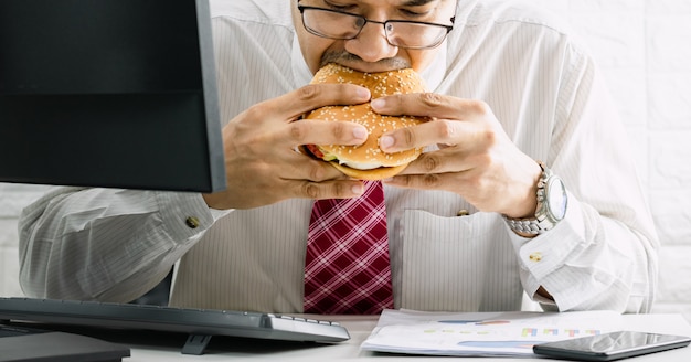 Les hommes qui travaillent n'ont pas le temps de manger d'urgence un hamburger de malbouffe tout en travaillant au bureau