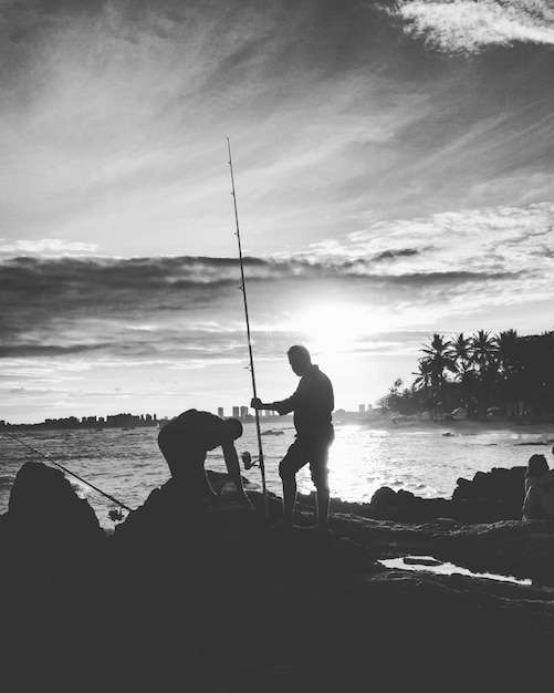 Photo des hommes en silhouette pêchant sur la plage contre le ciel