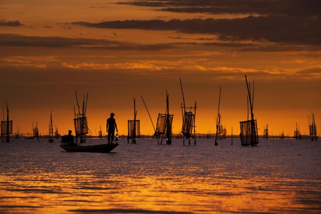Des hommes en silhouette sur un voilier en mer contre le ciel au coucher du soleil