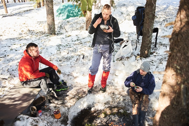 Hommes, touristes mangent dans la forêt près d'un feu