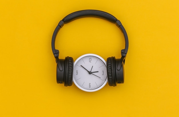 Horloge blanche avec casque stéréo noir sur fond jaune. Vue de dessus