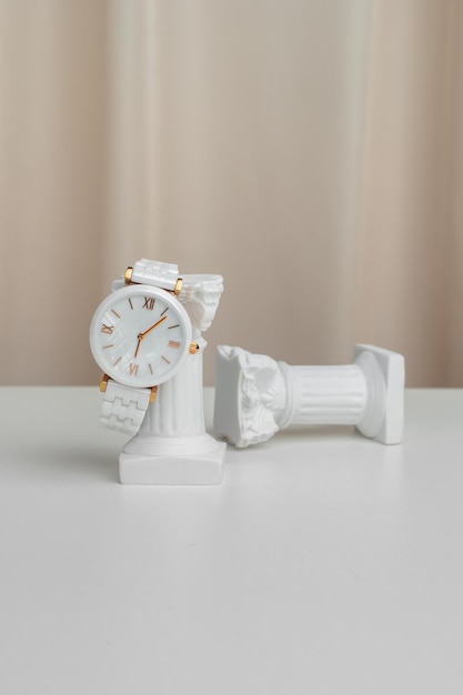 Une horloge blanche se trouve sur une colonne antique sur fond d'accessoires de luxe en tissu beige