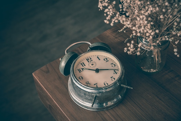 Horloge classique cassée sur la table en bois avec vase de fleurs séchées, notion de passage du temps.