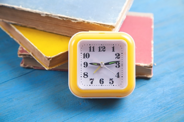 Horloge jaune et livres sur table en bois bleu.