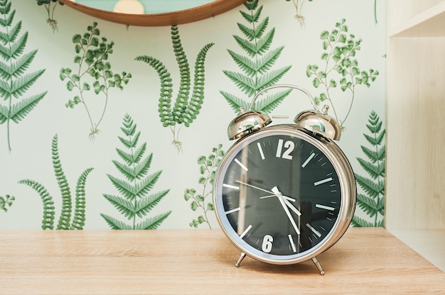 Horloge en métal chromé sur une table contre un mur avec un motif floral vert