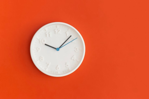 Horloge murale blanche sur fond rouge.