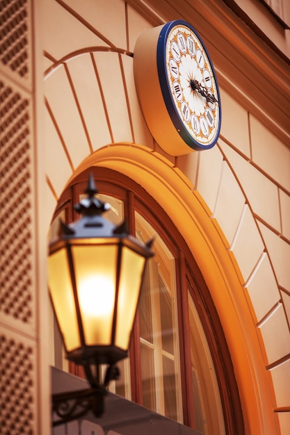 Horloge Murale Et Lampadaire Le Soir. Lampadaires Très éclairés Au Coucher Du Soleil. Lampes Décoratives. Lampe Magique Avec Une Lumière Jaune Chaude Dans Le Crépuscule De La Ville