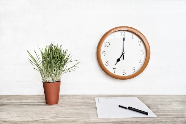 Horloge ronde sur un mur blanc, plante d'intérieur verte et une feuille de papier vierge avec un stylo