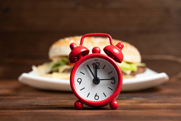 Photo horloge rouge et burger sur une plaque blanche et fond en bois.