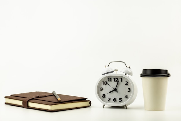 Horloge, tasse à café, crayon et un cahier en cuir sur un fond de bureau blanc avec espace de copie. - fournitures de bureau ou concept d’éducation.