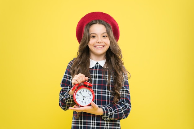 L'horloge tourne Petit enfant souriant avec une horloge mécanique sur fond jaune Adorable enfant avec de longs cheveux bruns et une horloge de réveil Bonne petite fille tenant un réveil