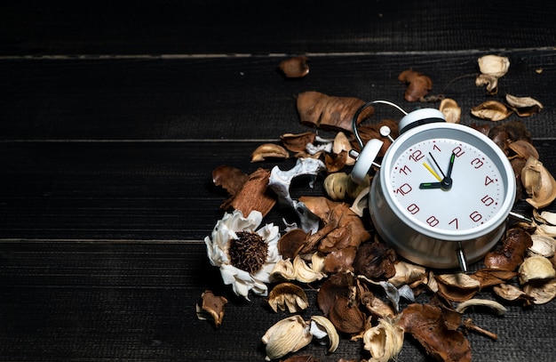 Horloge vintage blanche sur feuilles séchées sur une table en bois rétro noire