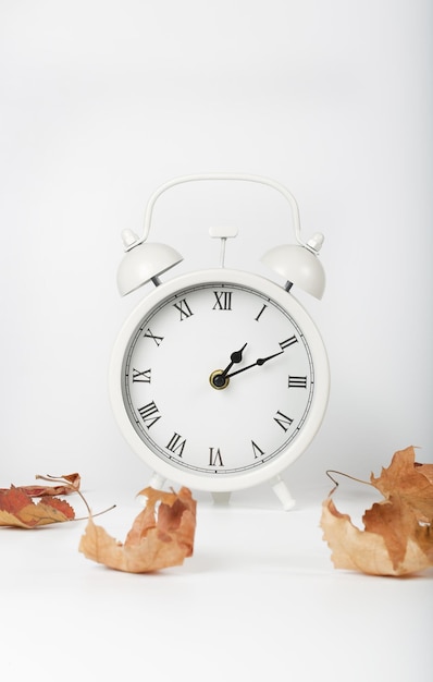 Horloge vintage blanche sur une surface grise entourée de feuilles séchées