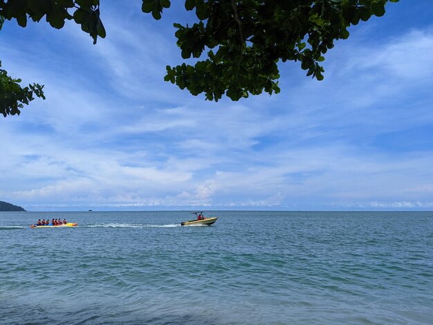 Un hors-bord tire un bateau banane qui est monté par des visiteurs en vacances sur une plage ici