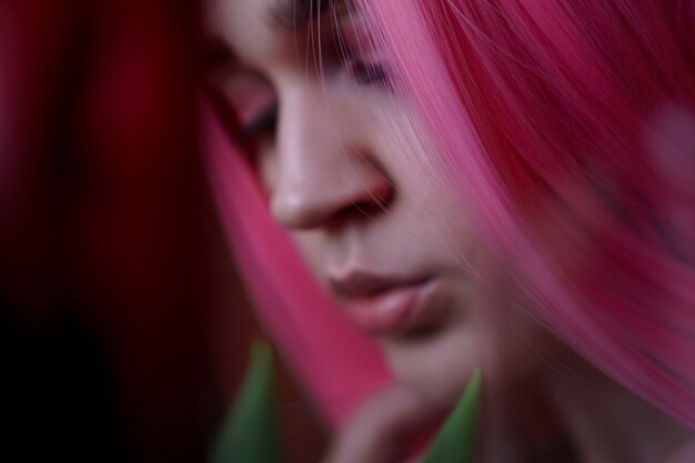 Hors mise au point, arrière-plan flou. Portrait d'une fille rêveuse aux cheveux rose vif avec des fleurs près du visage. Regarder sur le côté