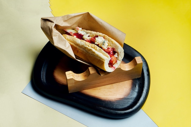 Hot-dog américain classique appétissant avec oignons caramélisés, fromage cheddar, moutarde et ketchup avec un plat de pommes de terre sur une surface colorée Restauration rapide