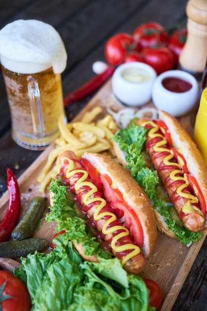 Hot-dog barbecue servi avec légumes et frites et sauces sur planche de service en bois