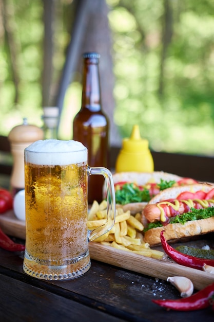 Hot-dog barbecue servi avec légumes et frites et sauces sur planche de service en bois