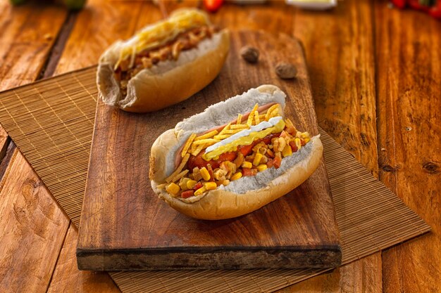 Hot-dog brésilien traditionnel sur une planche en bois avec des ingrédients autour.