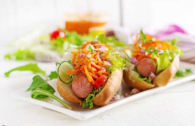 Hot-dog avec concombre, carotte, tomate et laitue sur table en bois.